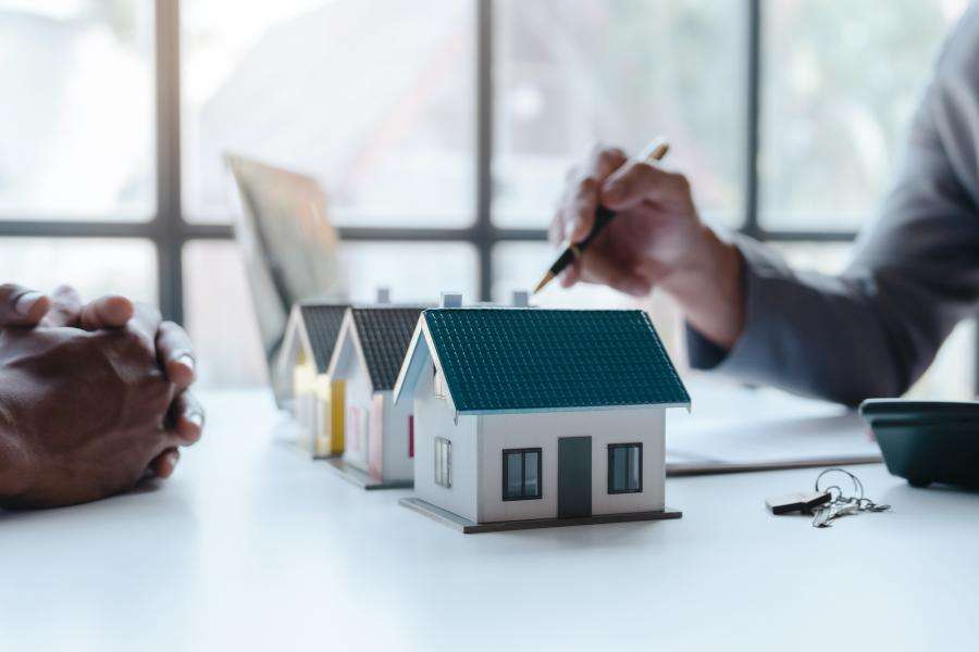 Two people observing house models, pointing with a pen to depict a discussion of what is happening with the housing market