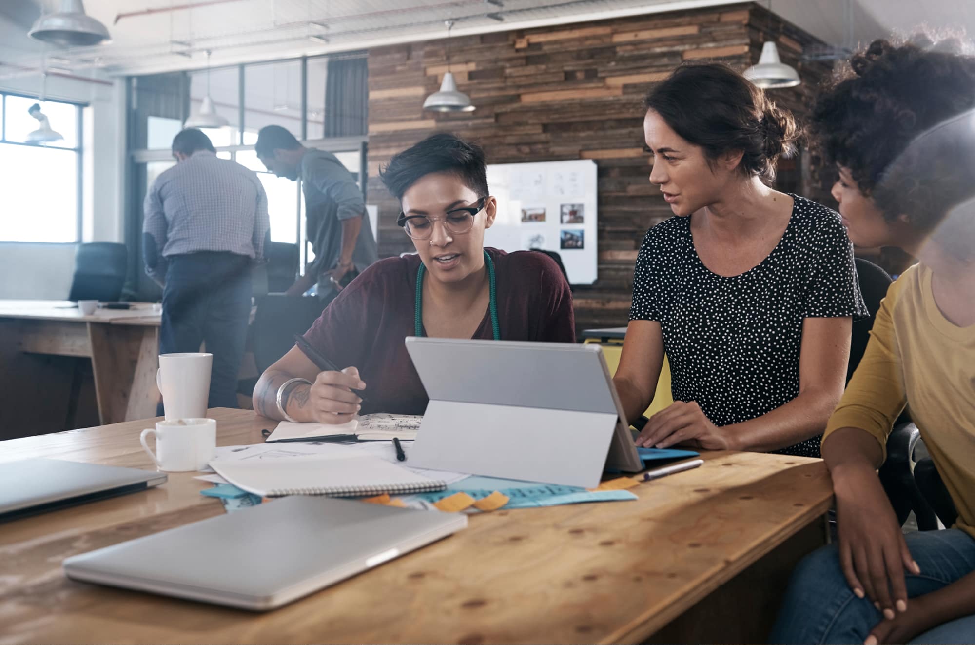Three women are in a coffee shop looking at a computer together. | The CE Shop