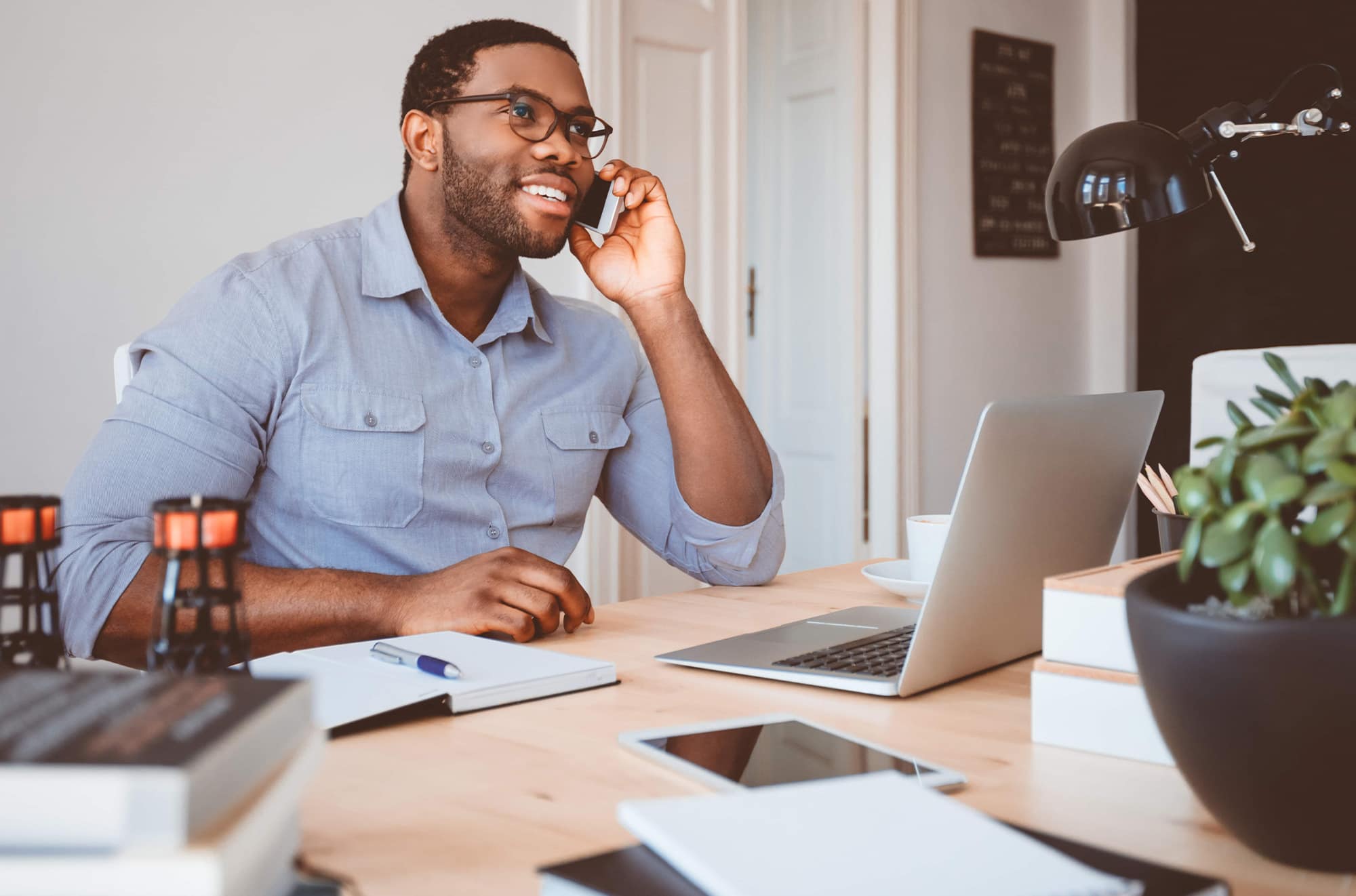 A man is sitting at a desk, he is on the phone.