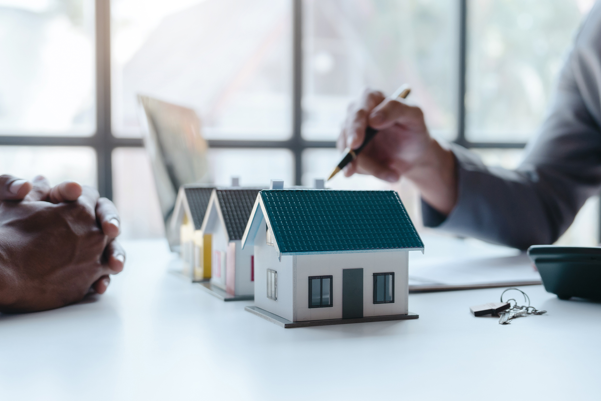 Two people observing house models, pointing with a pen to depict a discussion of what is happening with the housing market