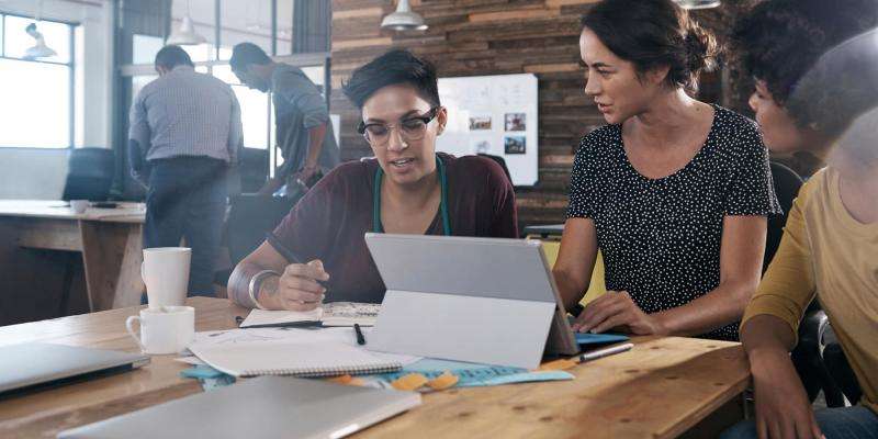 Three women are in a coffee shop looking at a computer together. | The CE Shop