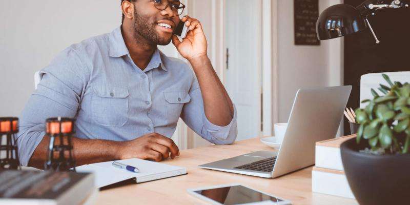 A man is sitting at a desk, he is on the phone.