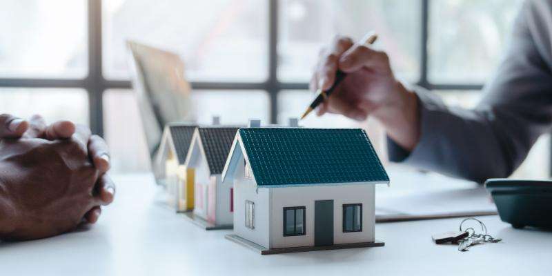 Two people observing house models, pointing with a pen to depict a discussion of what is happening with the housing market